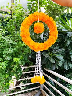 an orange and white flower decoration hanging from a wooden rail in front of some trees