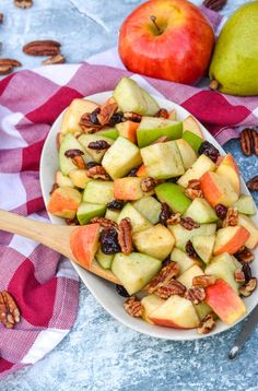 a white bowl filled with apples and pecans on top of a checkered table cloth