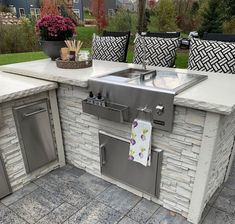 an outdoor kitchen with stainless steel appliances and seating on the outside patio, next to a potted plant