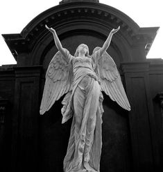 an angel statue is standing in front of a building with its arms spread wide open