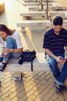 two people sitting on a bench looking at their cell phones while one person sits next to them