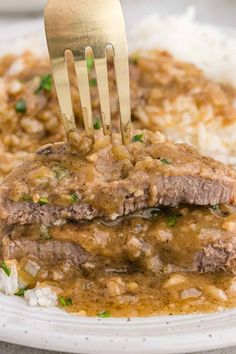 a fork sticking out of some meat and rice on a plate with gravy