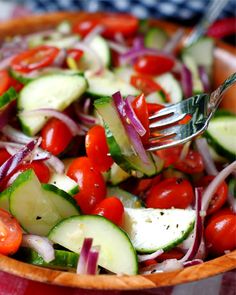 a wooden bowl filled with cucumbers, tomatoes and onions next to a fork