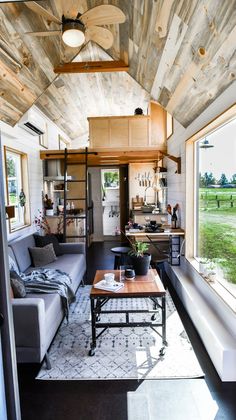 a living room filled with furniture next to a window and a wooden ceiling mounted on the side of a wall