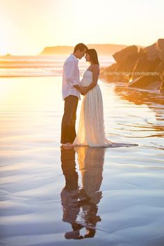 a pregnant couple standing in the water at sunset