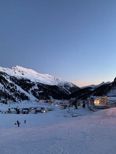 two people skiing down a snow covered slope at night with mountains in the background and houses lit up