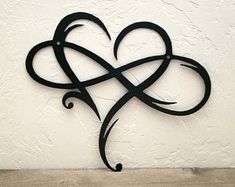 a metal heart with an intricate design on the side of a white wall next to a wooden table