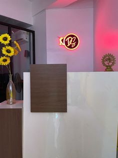 a vase filled with yellow flowers sitting on top of a counter next to a neon sign