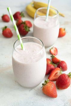 two glasses filled with milk and strawberries next to bananas