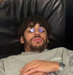 a man laying on top of a black leather chair with his eyes covered by purple hearts