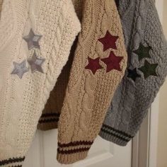 three knitted mittens hanging from a hook on a white door with silver stars