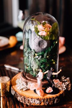 a glass dome with flowers and greenery in it on a wooden table next to other items