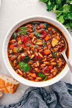 a white bowl filled with vegetable soup next to bread and parsley on the side