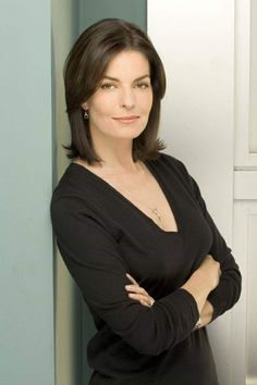 a woman leaning against a wall with her arms crossed and looking at the camera while wearing a black top