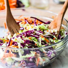 two wooden spoons in a glass bowl filled with coleslaw and carrots