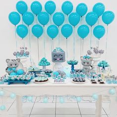 a table topped with lots of blue balloons and desserts next to a white wall