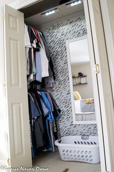 an open closet with clothes hanging on the wall and a laundry basket in front of it