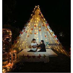 a man and woman sitting in front of a lit up teepee with hearts on it