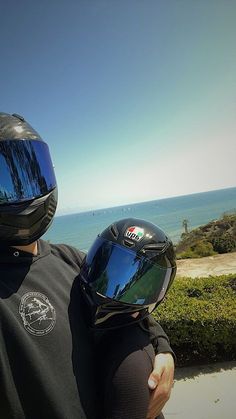 a man wearing a motorcycle helmet and holding onto his child's back with the ocean in the background