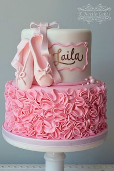 a pink cake with ballet shoes and name written on the top, sitting on a pedestal