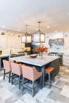 a kitchen with white cabinets and an island in the middle, surrounded by orange chairs