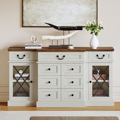 a white cabinet with drawers and two vases on top, in front of a painting