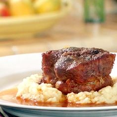 a white plate topped with meat and gravy on top of mashed potatoes