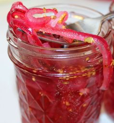 a jar filled with red liquid sitting on top of a white table next to a spoon