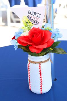 a red rose is in a baseball vase on a blue tablecloth with a sign