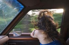 a woman sitting in the passenger seat of a car with her hair blowing in the wind