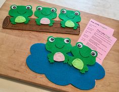 three felt frog puppets sitting on top of a wooden board