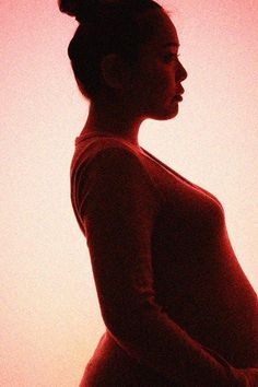 a pregnant woman standing in front of a pink sky