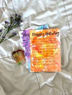 two greeting cards sitting on top of a bed next to a bottle of water and flowers