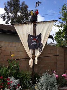 a pirate flag hanging on the side of a building with flowers in front of it