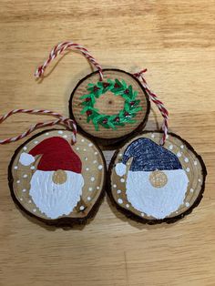 three wooden ornaments with santa and snowman faces on them, hanging from twine strings