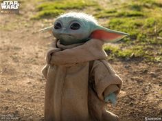 a baby yoda doll standing in the dirt with its arms wrapped around it's head