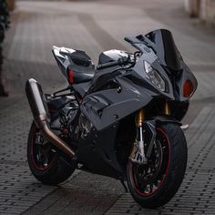 a black motorcycle parked on the side of a road next to a brick sidewalk with red rims