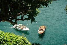 two small boats floating on top of a body of water next to lush green trees