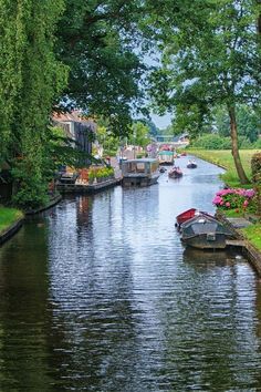 boats are lined up along the side of a narrow canal in an area with green grass and trees