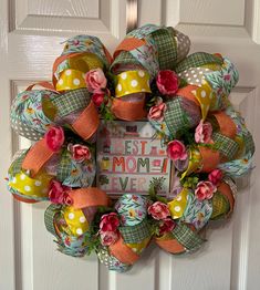 a wreath with flowers and ribbons hanging on the front door for mom's day