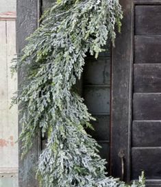 a wreath is hanging on the door of an old building with snow and pine needles