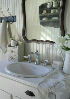 a white sink sitting under a bathroom mirror next to a vase with flowers in it