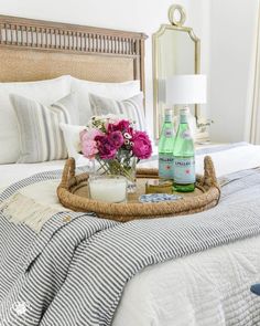 a tray with flowers on top of a bed next to two bottles of water and a candle