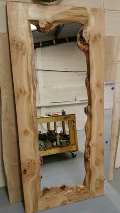 a wooden mirror sitting on top of a floor next to a table with a bird perched on it