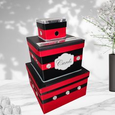 three red and black boxes stacked on top of each other next to a vase with flowers