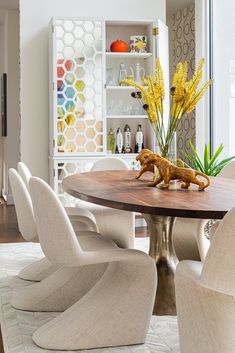 a dining room table with white chairs and yellow flowers in vases on the top