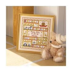 a teddy bear sitting next to a framed cross - stitch sample in front of a door