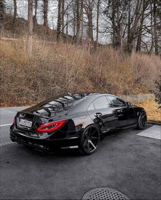 a black car parked in the parking lot next to some bushes and trees with no leaves on them