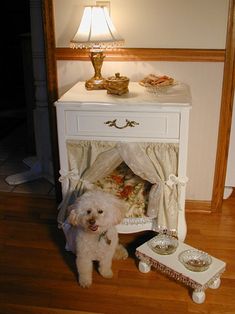 a white dog sitting in its bed under a table with a lamp on top of it