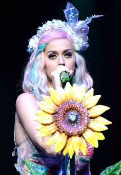 lady with sunflower in front of black background wearing costume and headdress, holding microphone up to her mouth